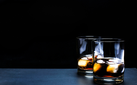 Два стакана с виски и льдом на тёмной поверхности, чёрный фон